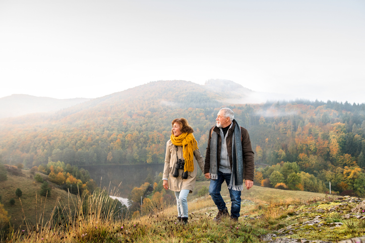A senior couple walking in the mountains who is downsizing to save their retirement.
